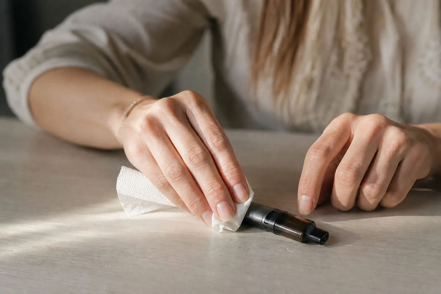 Mains essuyant quelques gouttes de liquide à la base d'une cigarette électronique