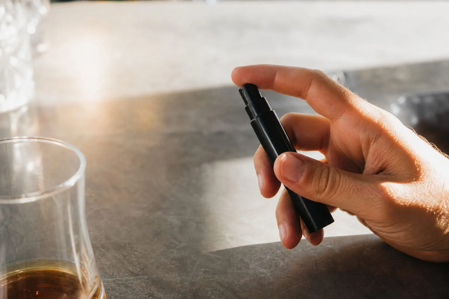Un stylo vaporisateur noir tenu entre deux doigts, fond neutre lumineux