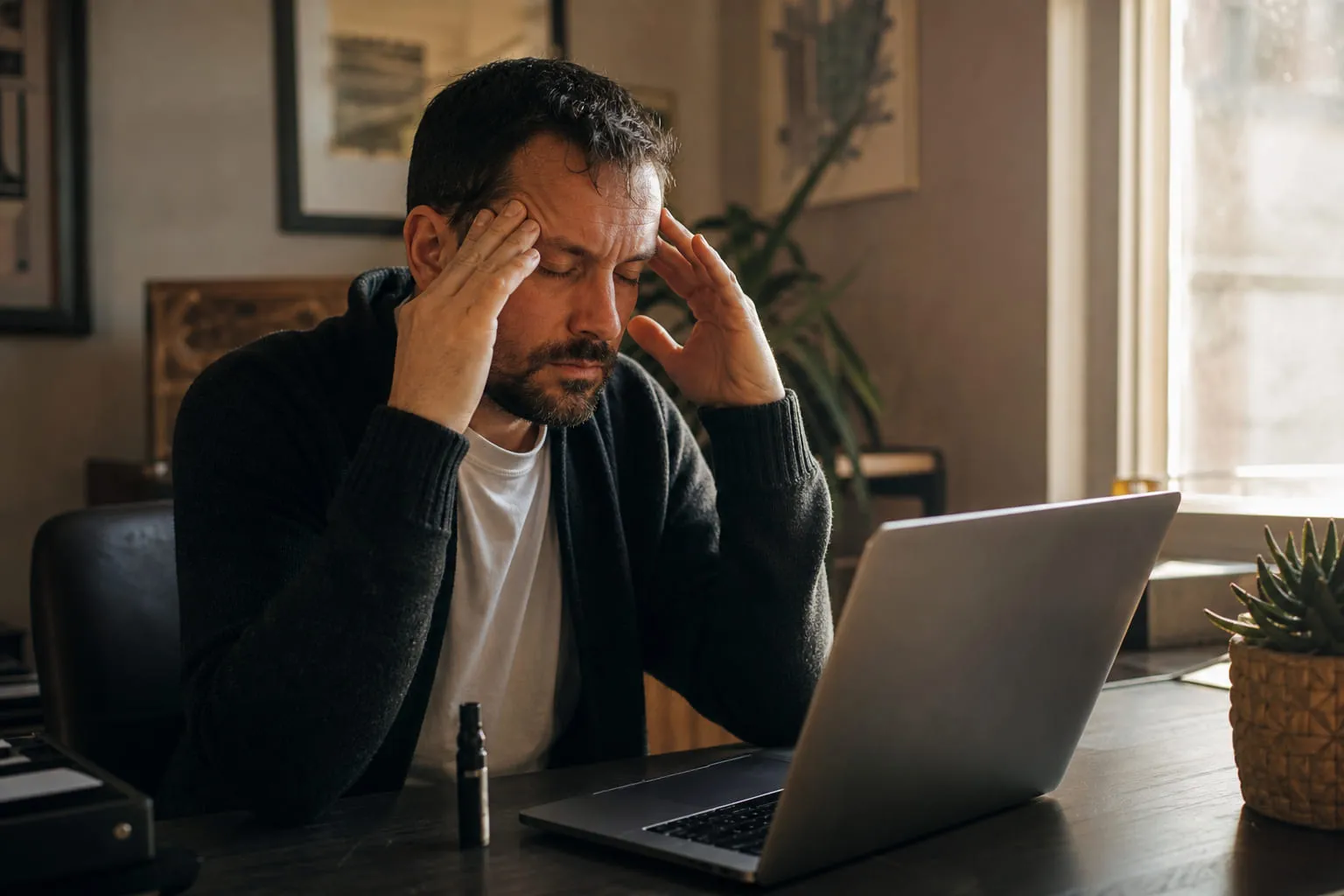 Homme se massant les tempes à son bureau, cigarette électronique près du clavier