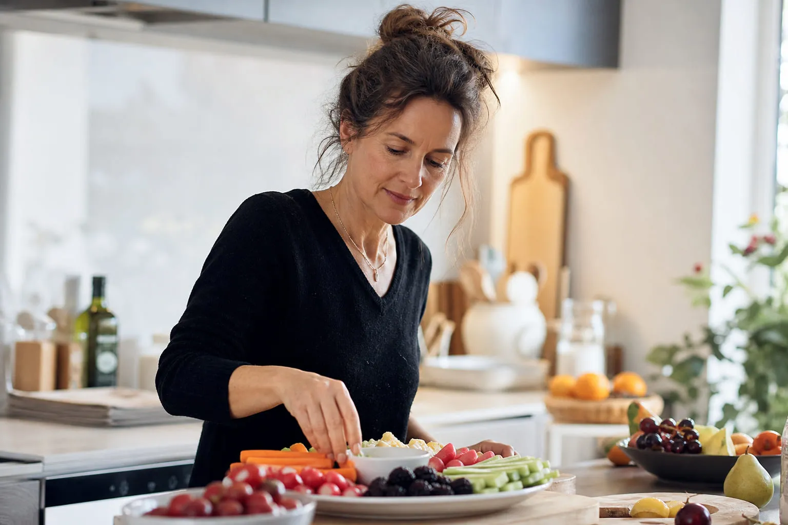 Femme préparant une assiette de légumes et de fruits dans une cuisine claire