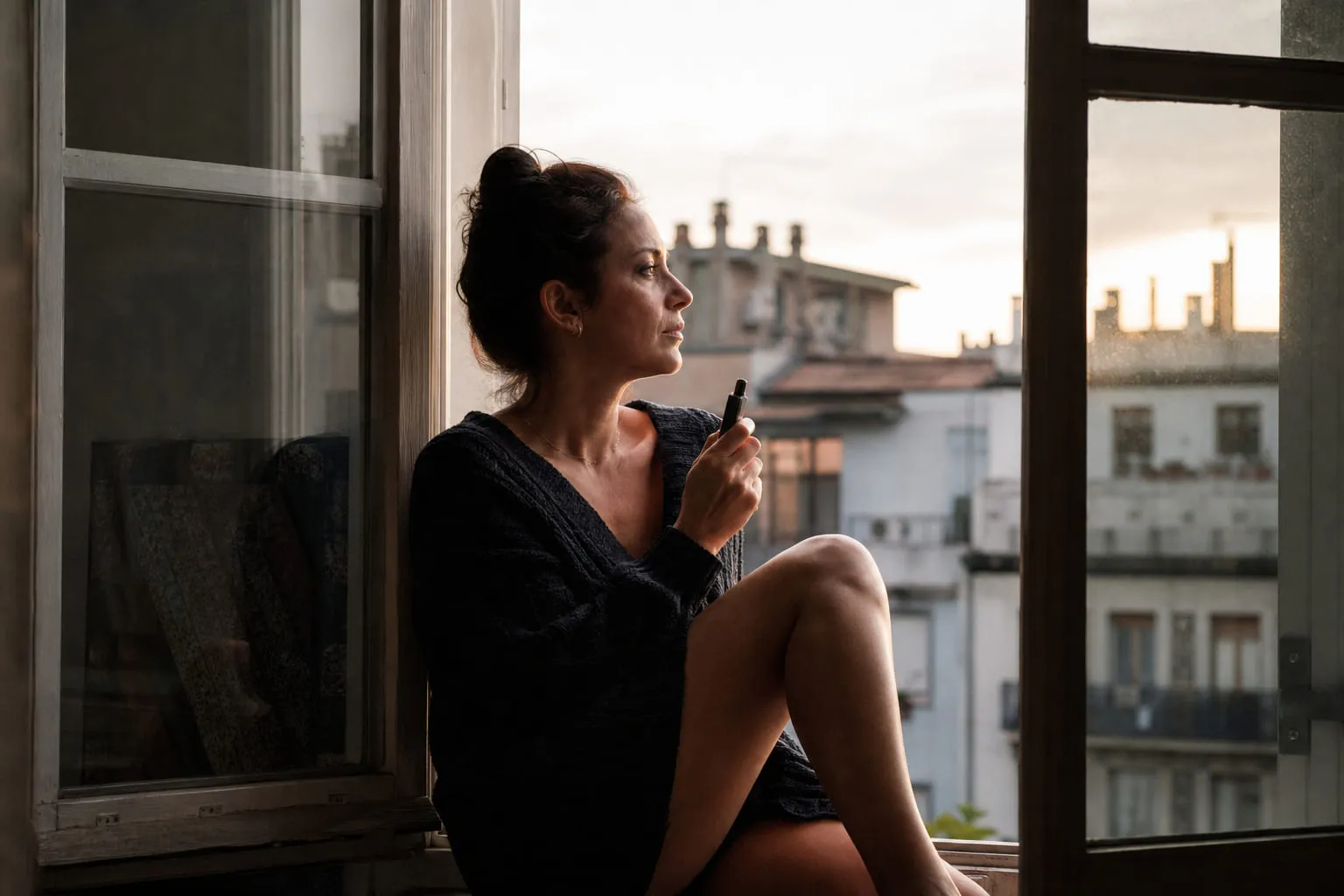 Femme pensive au bord d'une fenêtre, cigarette électronique à la main