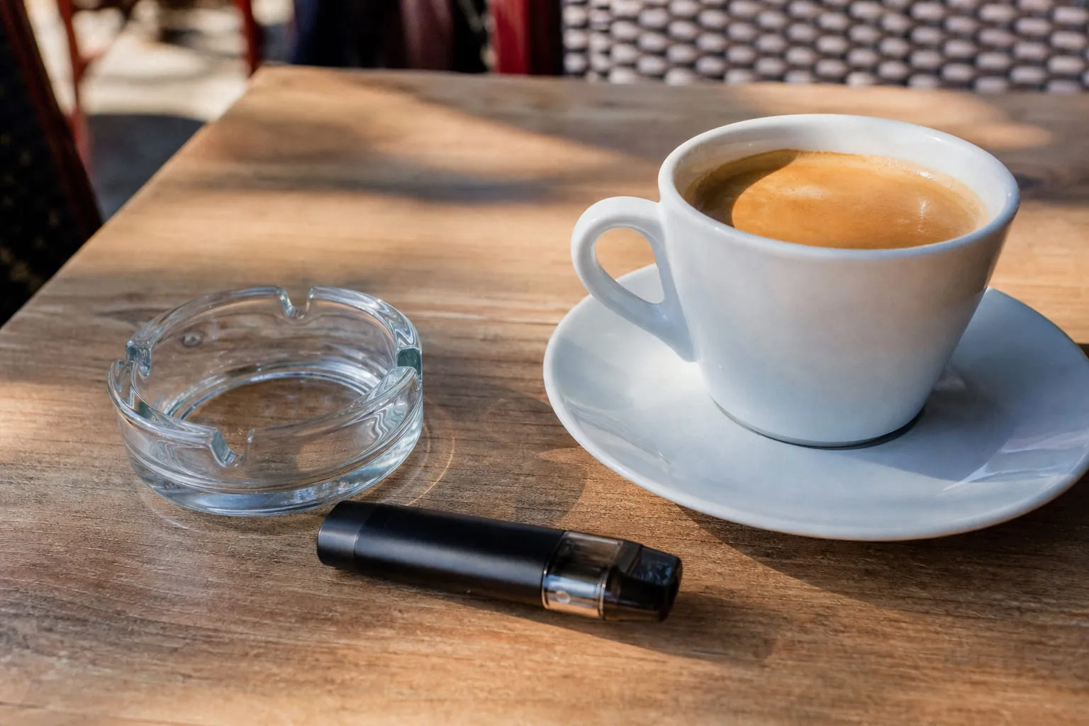 Cendrier vide et cigarette électronique posés à côté d'une tasse de café en terrasse