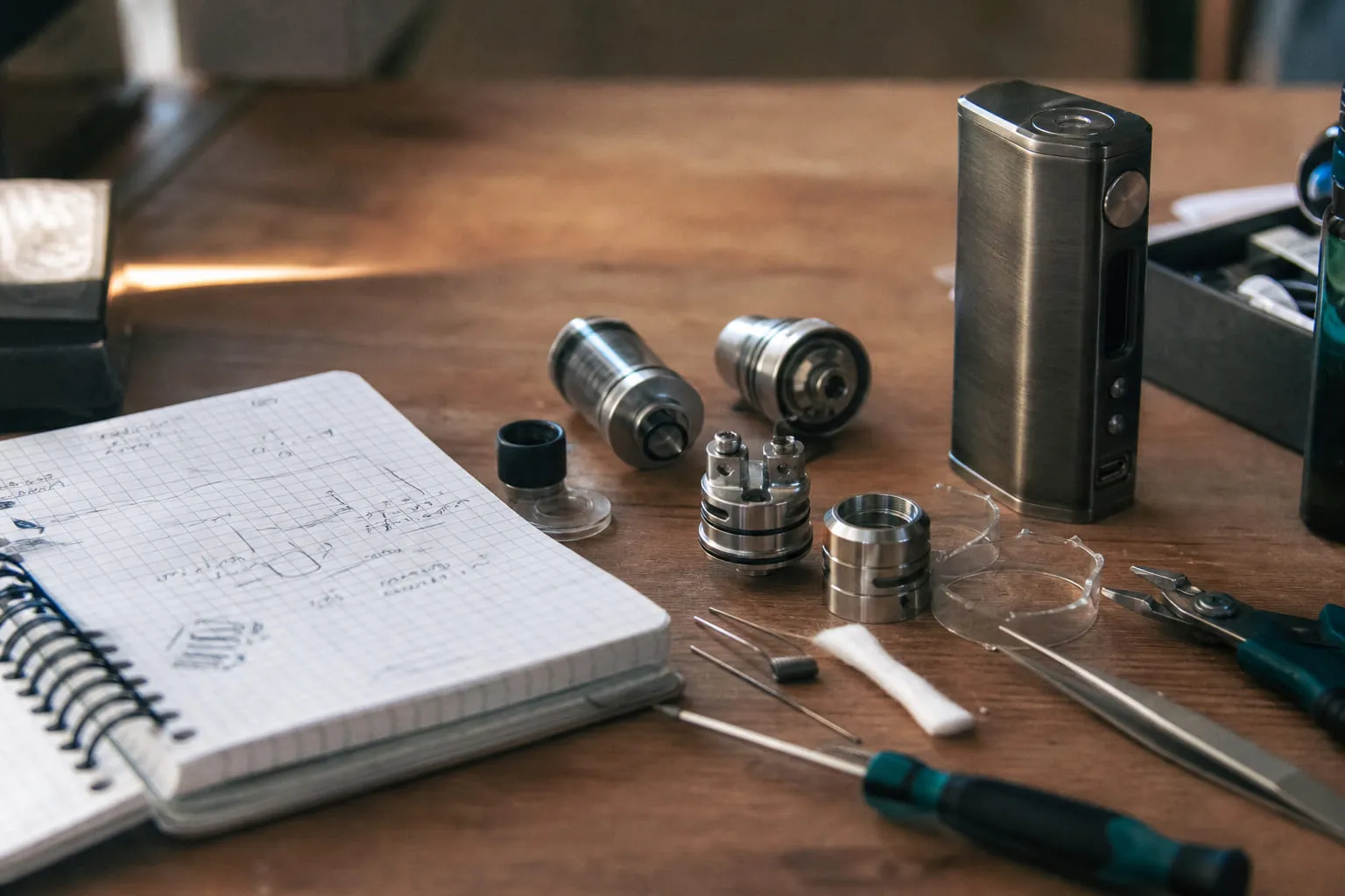 Box mod et atomiseur posés sur un établi en bois avec des outils